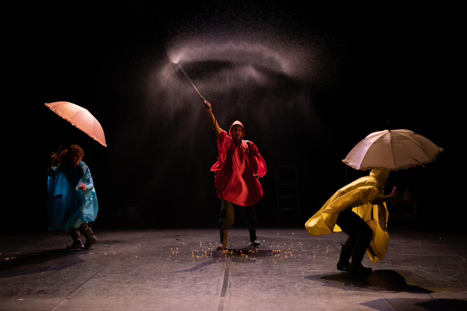 In foto, un uomo con impermeabile rosso agita una bacchetta che spruzza acqua. Vicino a lui altre due persone con impermeabili e ombrelli.
