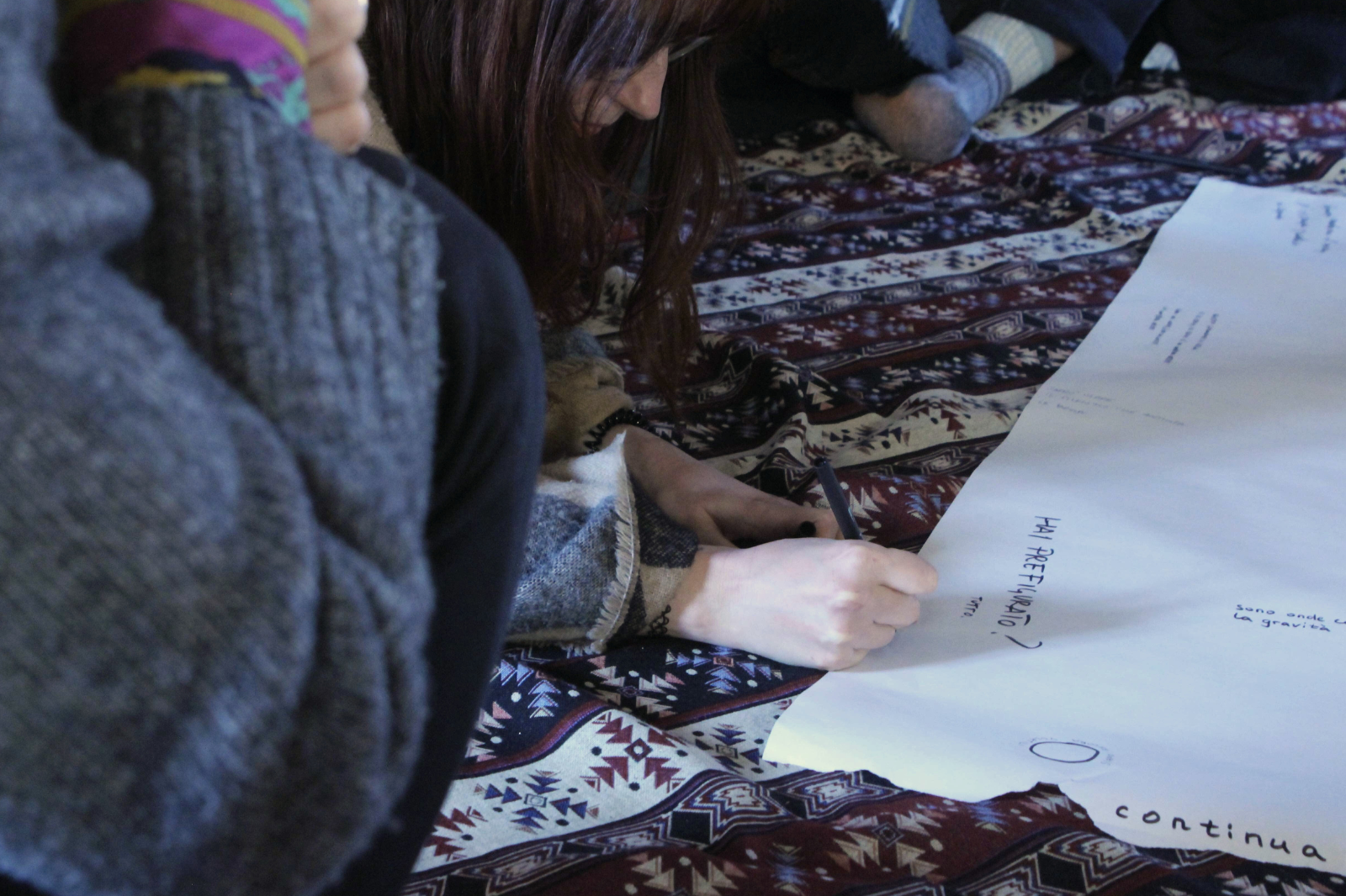 Una ragazza, accovacciata su un tappeto, scrive su un grande foglio bianco.