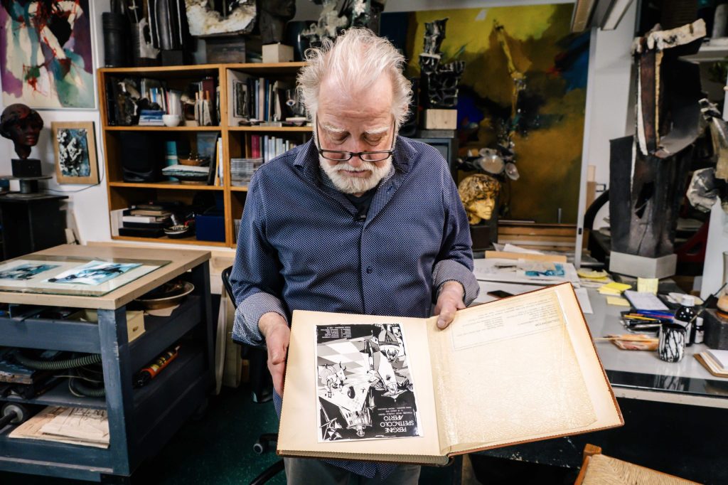Il pittore Ivo Fruet tiene in mano un libro pieno di fotografie storie.