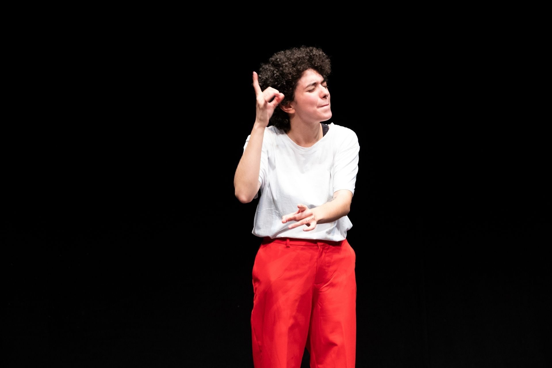 Il performer Diana Anselmo vestito di bianco e rosso parla in LIS.