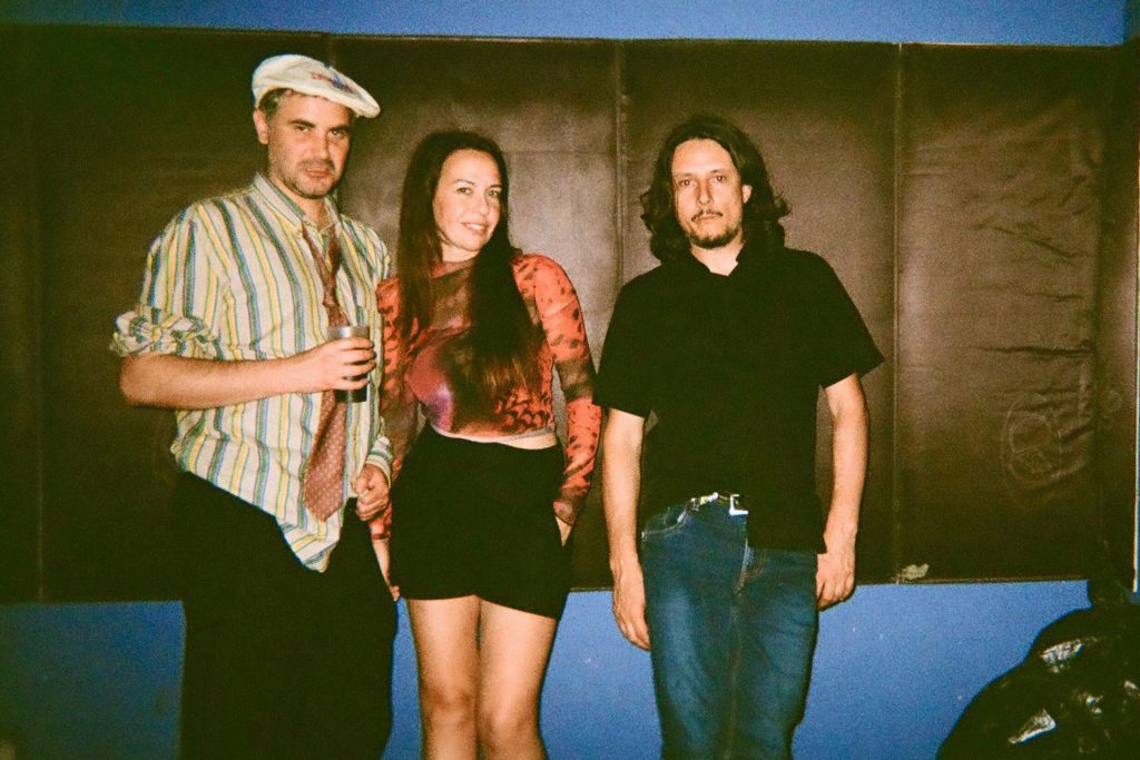 La band +39) 375-649-94-64 My Telephone Number, composta da due uomini e una donna, sorride in camera.