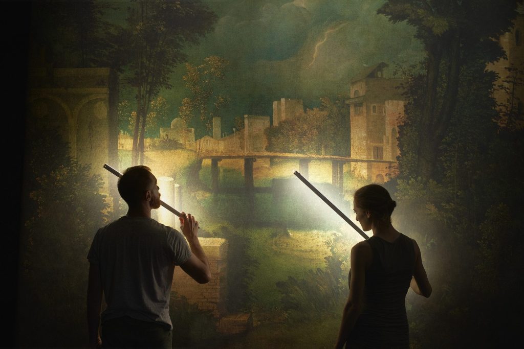 Sagome di un uomo e una donna di schiena, illuminano un dipinto di un paesaggio con lunghi fari led.