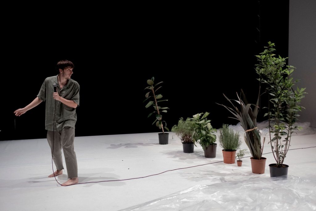 Un attore si gira destra e osserva sette piante.