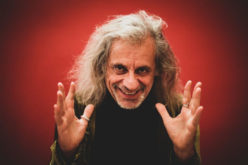 Su sfondo rosso, Alessandro Bergonzoni sorride.