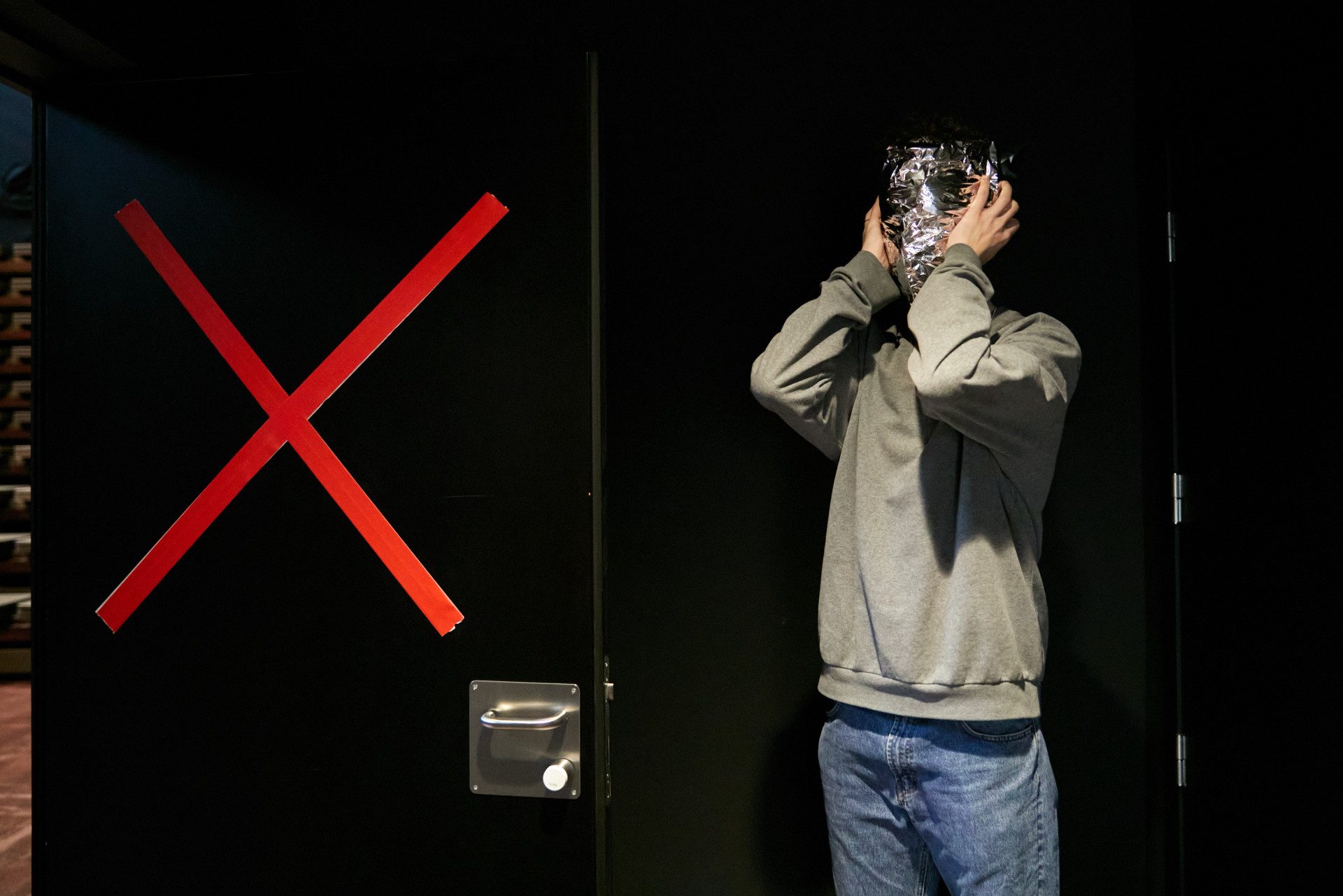 Un ragazzo in jeans e felpa, si tiene la testa tra le mani. La sua faccia è coperta da una maschera di stagnola.