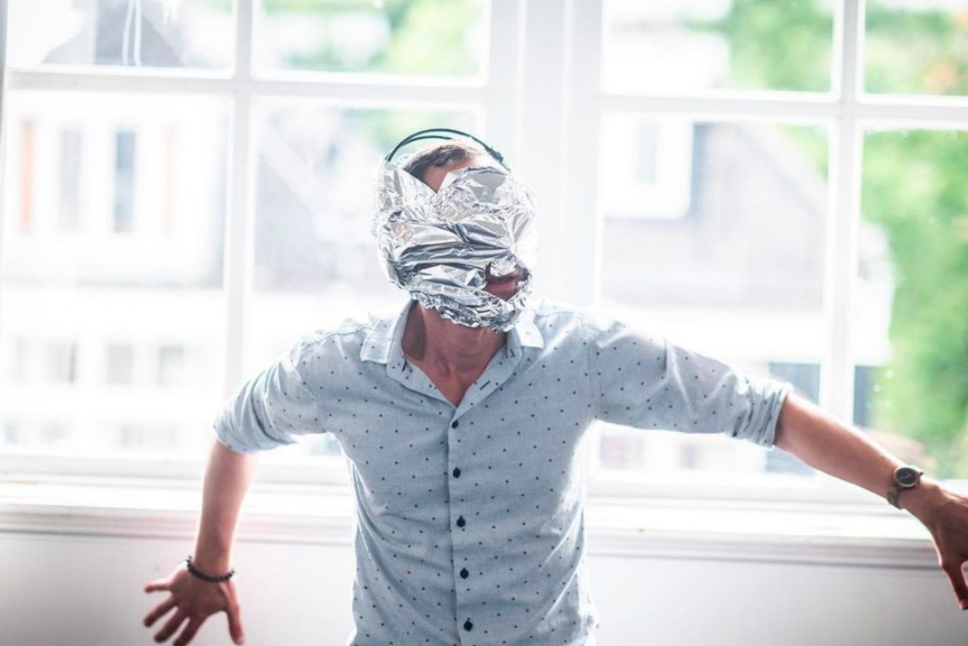 Un uomo vestito tiene le braccia aperte. La sua faccia è coperta da stagnola.