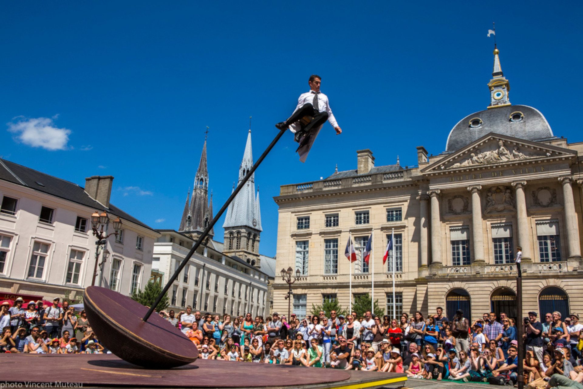 Il circense Vincent Martinez volteggia in aria, in mezzo a una piazza, aggrappato a un pendolo gigante.