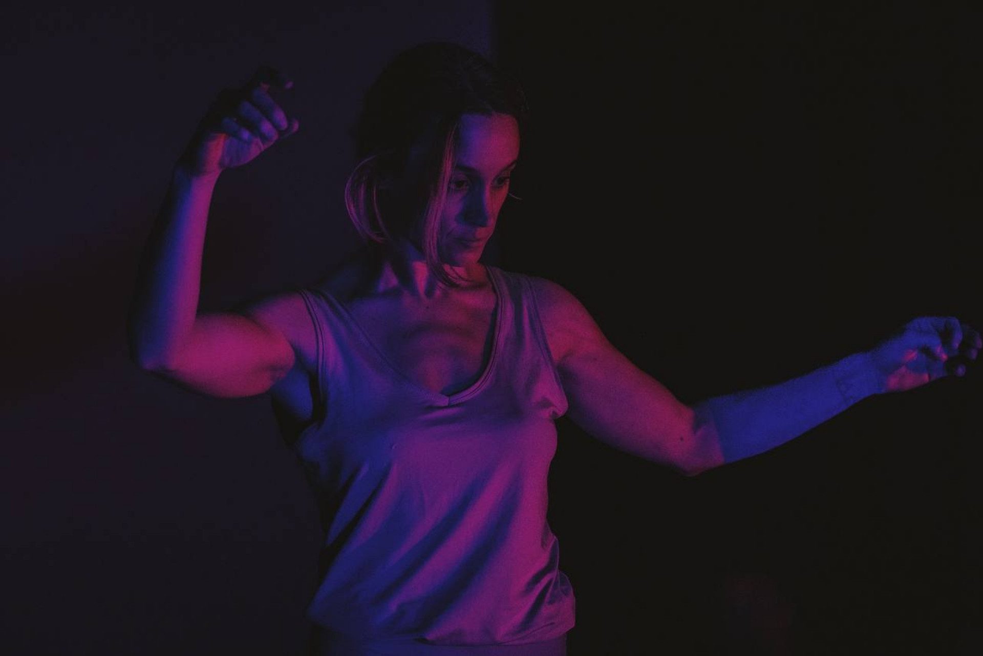 In ambientazione scura, una donna è illuminata da luce blu/rosa.