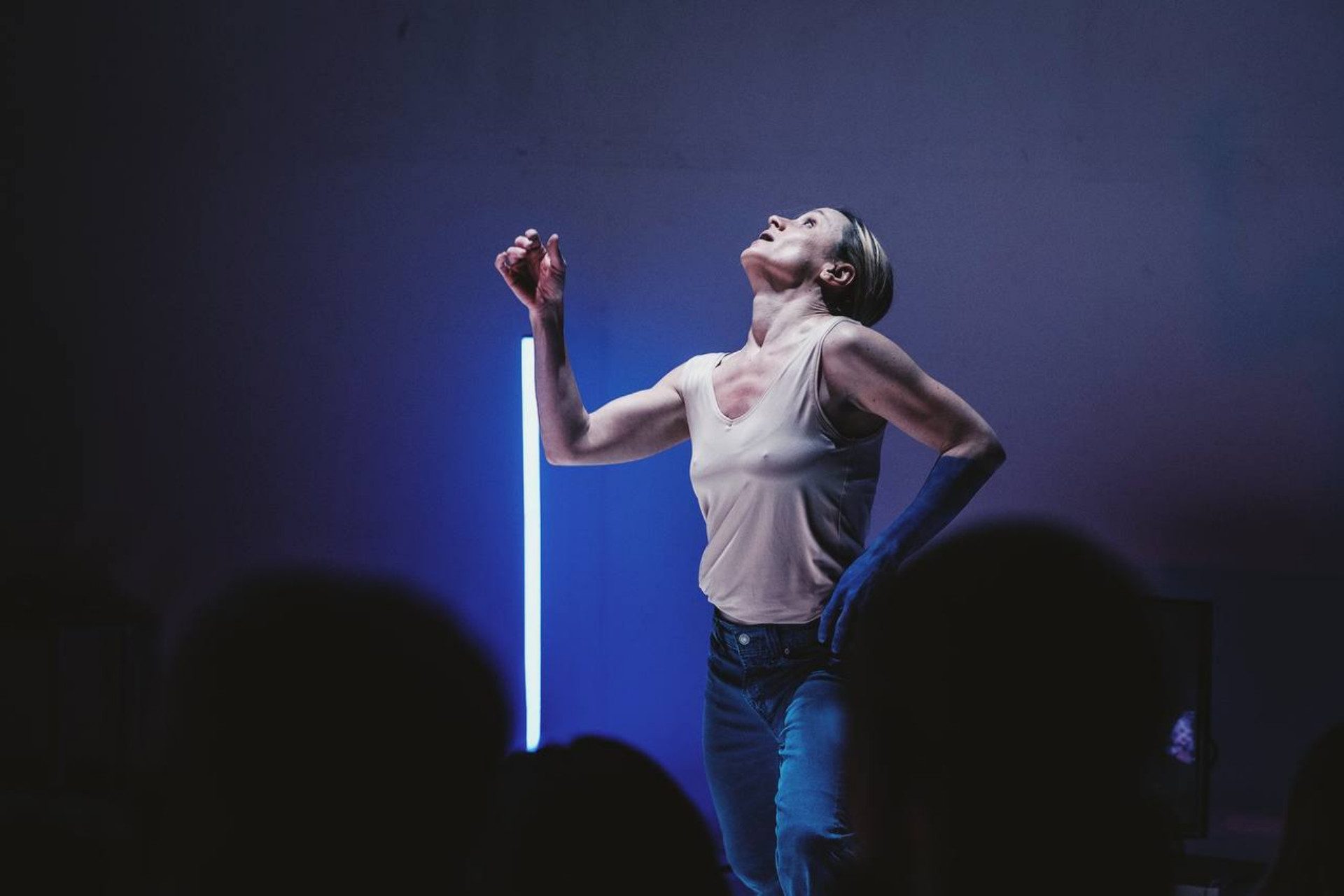 Un'attrice guarda verso l'alto con la mano destra alzata. Il braccio sinistro è blu.