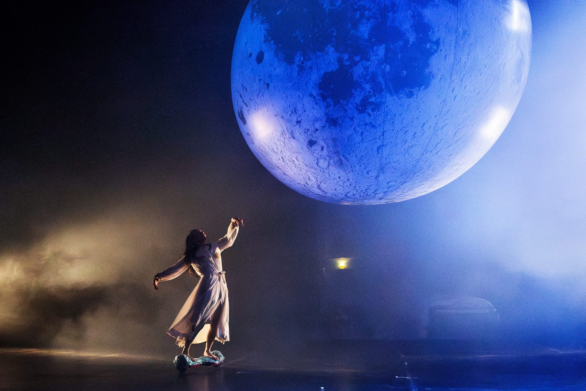 Una donna vestita con un vestito bianco balla sotto una grande luna piena.