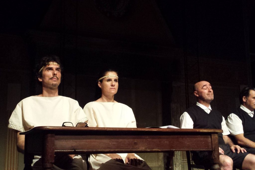 Gli attori interpretano gli dei dell'Olimpo seduti in mezzo ai banchi di scuola.