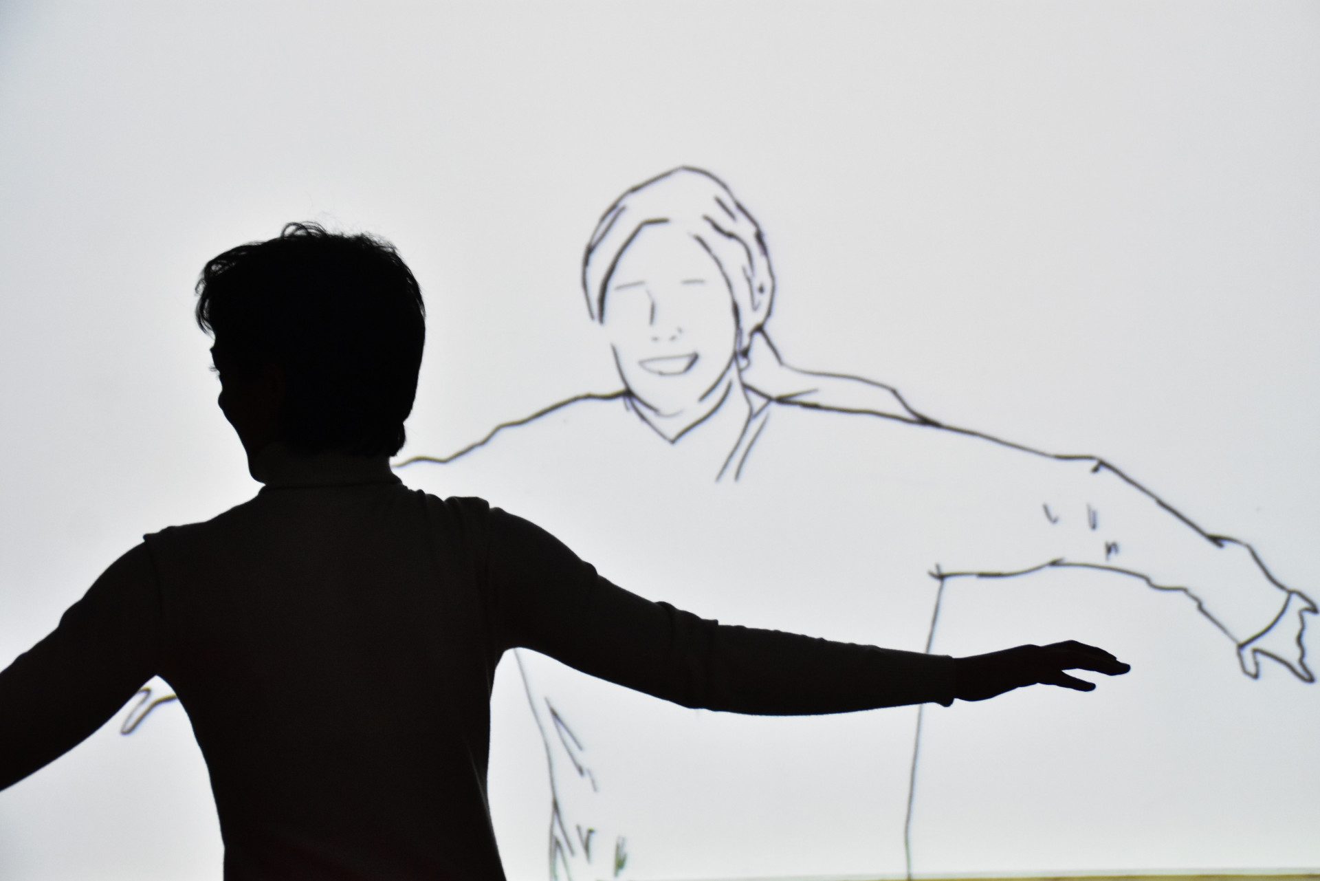 Sagoma di persona davanti a schermo bianco che proietta il disegno di una ragazza felice.