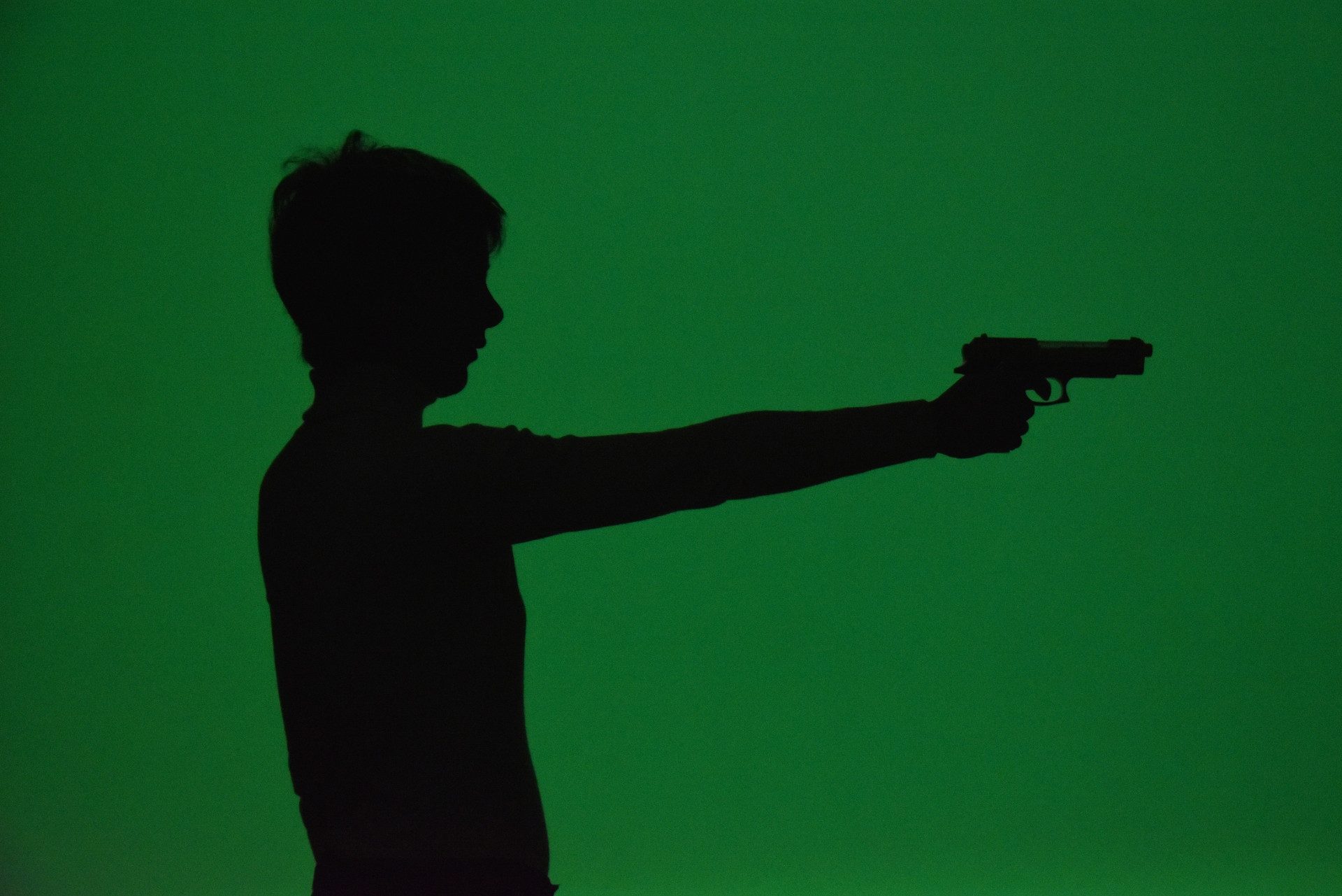 Sagoma controluce di una donna che impugna una pistola: tutto è verde.