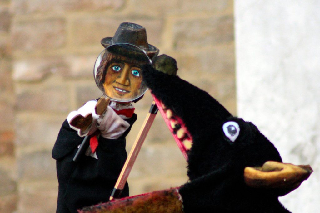 Due marionette: una è un uomo con cappello, l'altra un lupo che sta per mangiarlo.