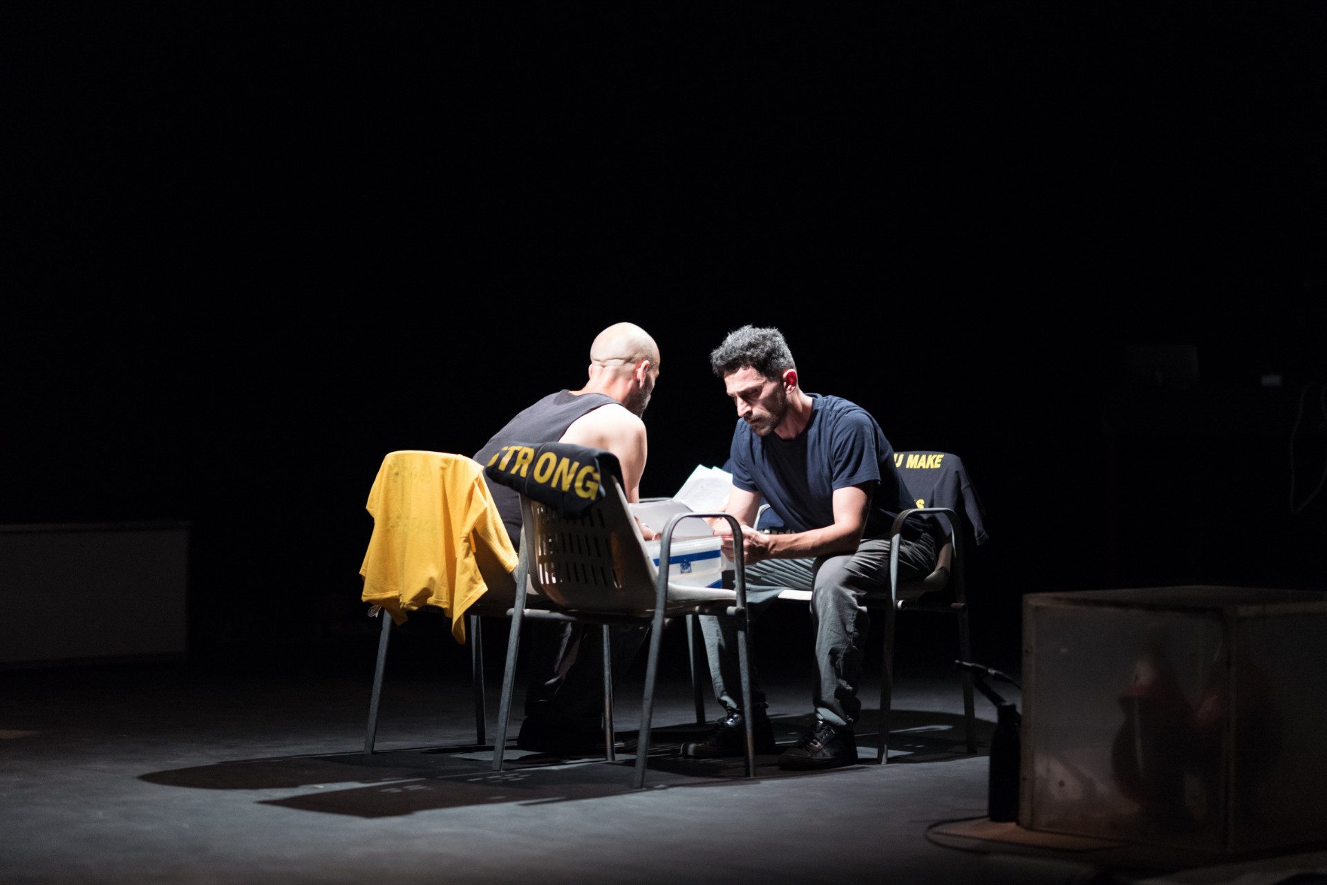 Due attori siedono uno di fronte all'altro con dei fogli in mano.