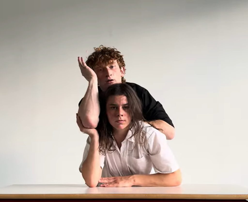 Gli artisti Emily Heather Manica e Linus Jansner, seduti a un tavolo, sorreggono l'una il braccio dell'altro.