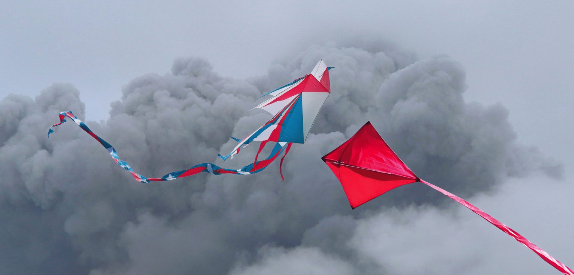 Due aquiloni colorati volano in una cielo pieno di nubi scure.