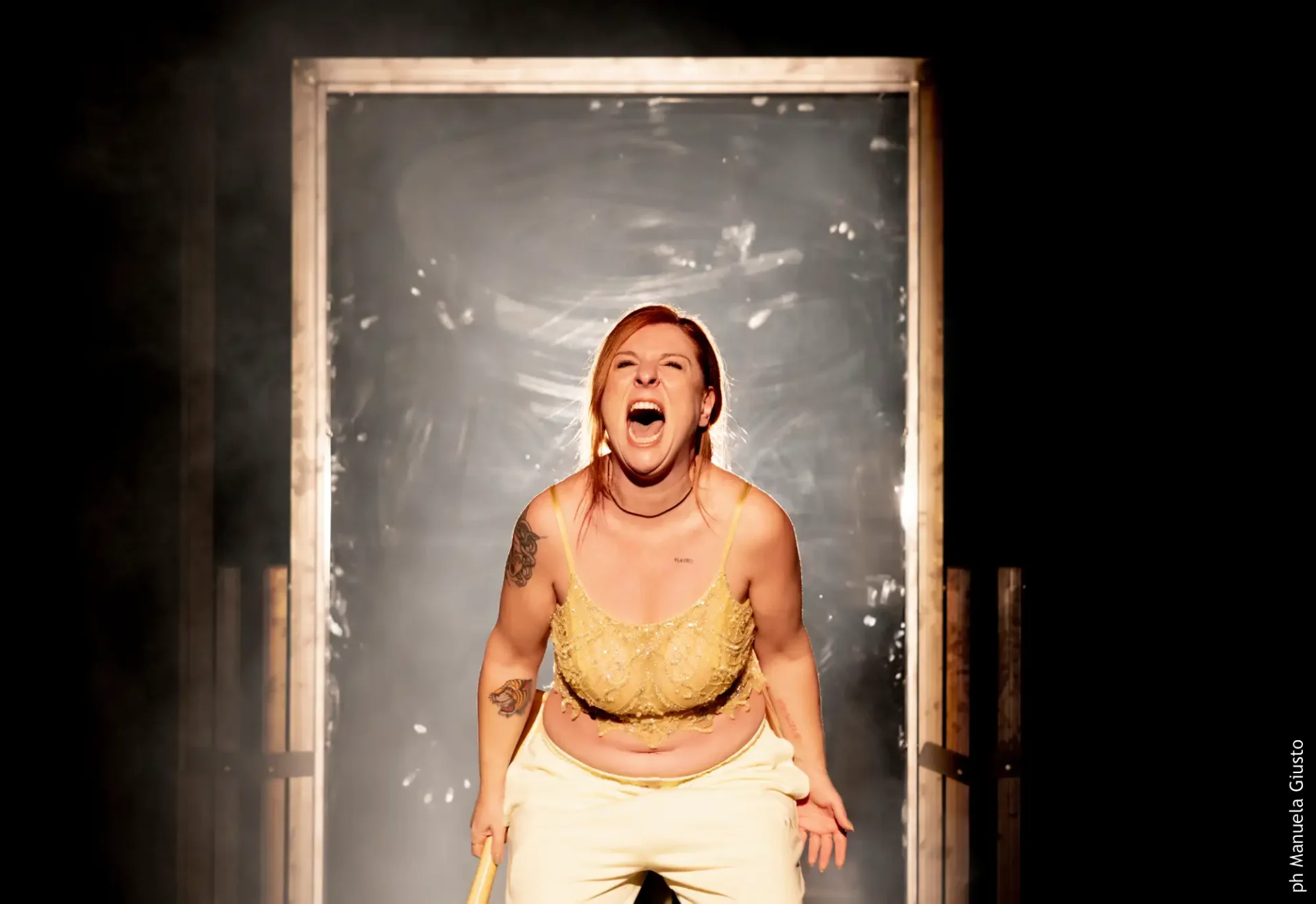 L'attrice Licia La Nera, indossa una canottiera dorato e pantaloni bianchi. I capelli rossi raccolti in una coda bassa. Urla, gli occhi sono chiusi.