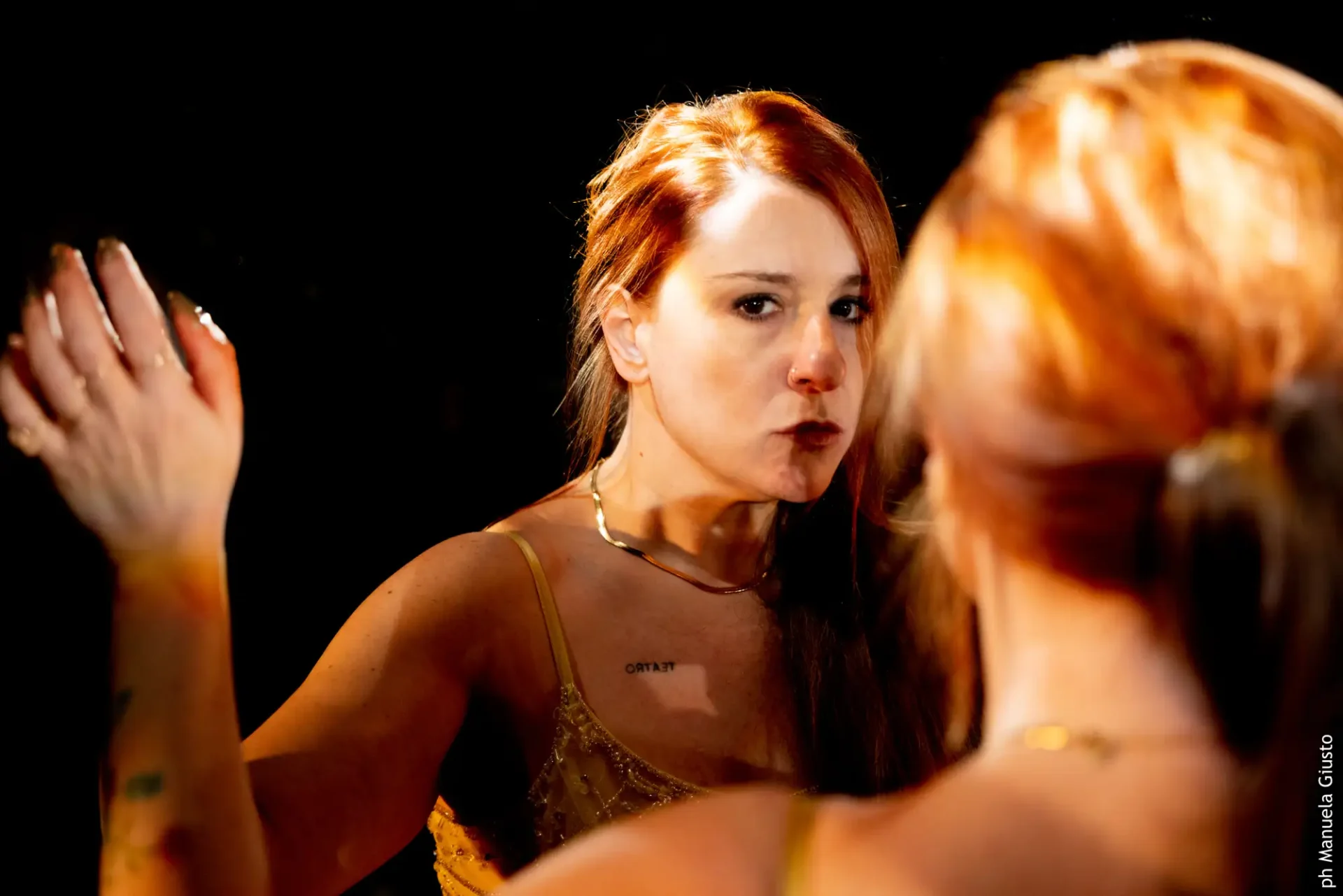 Licia La Nera, lunghi capelli rossi e raccolti in una coda bassa che le cade sulla spalla, si guarda allo specchio