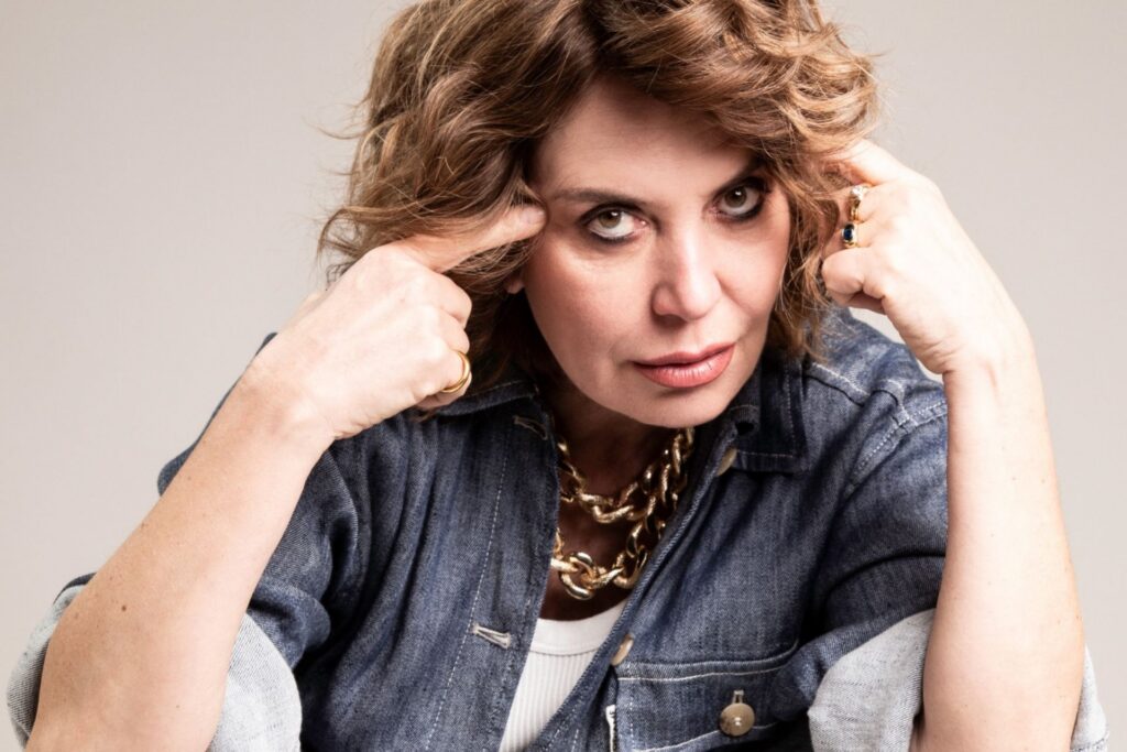 L'attrice Sabina Guzzanti guarda in camera indicandosi la tempia con il dito indice