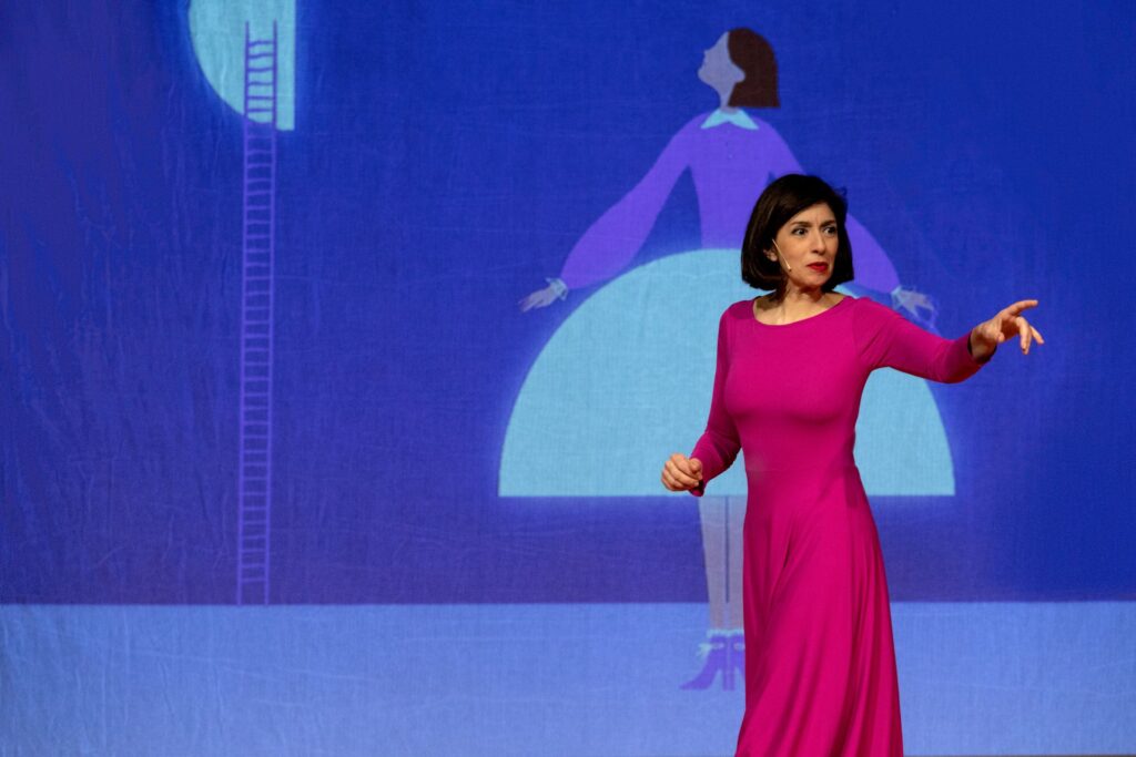 L'attrice Cinzia Spanò indica qualcosa, indossa un abito fucsia