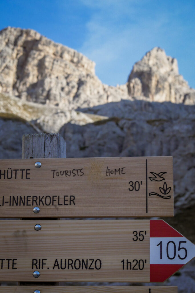 Su un cartello che segnala un percorso di trekking, la scritta a penna TOURISTS GO HOME. La scritta GO è stata cancellata. Sull sfrondo delle montagne.